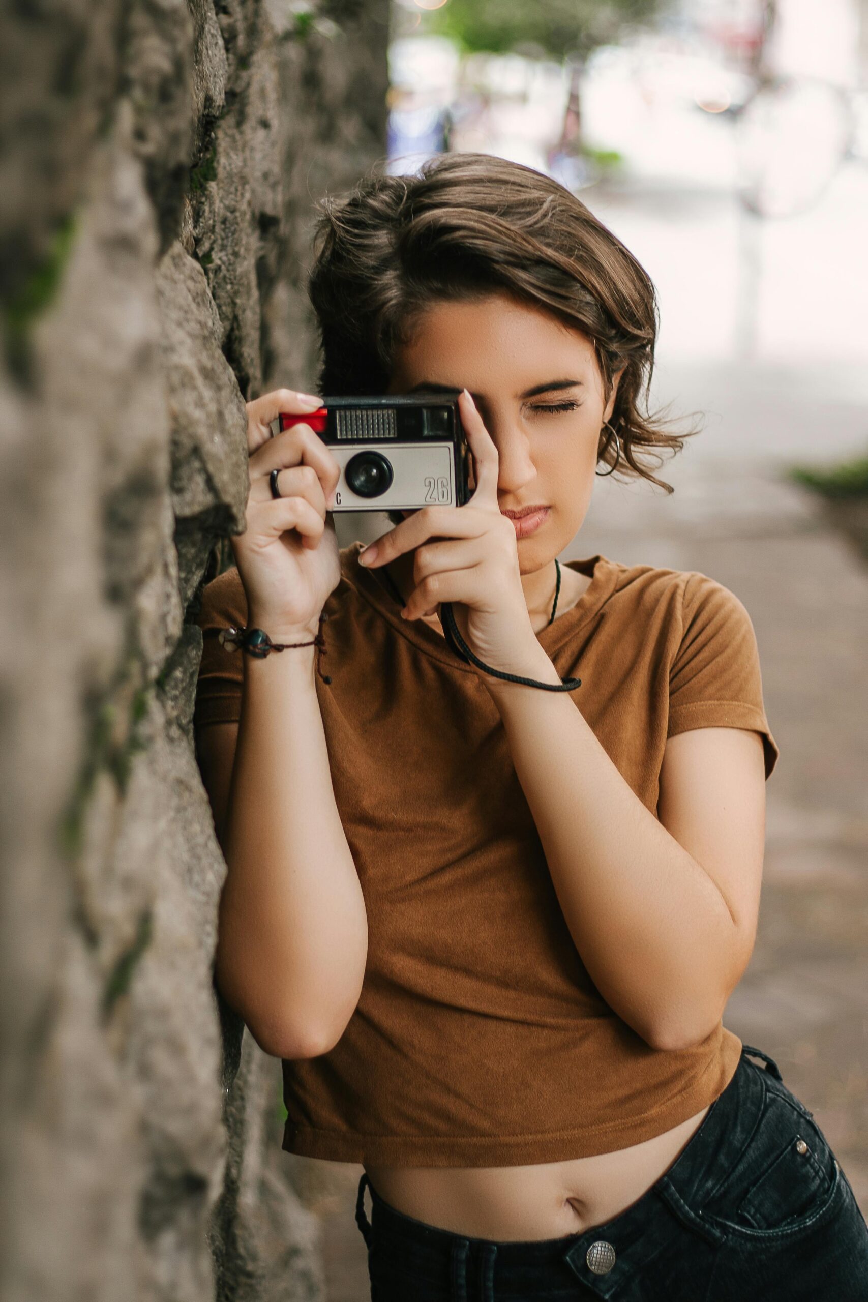 A young woman in São Paulo captures a moment using a vintage camera, embodying urban street style.